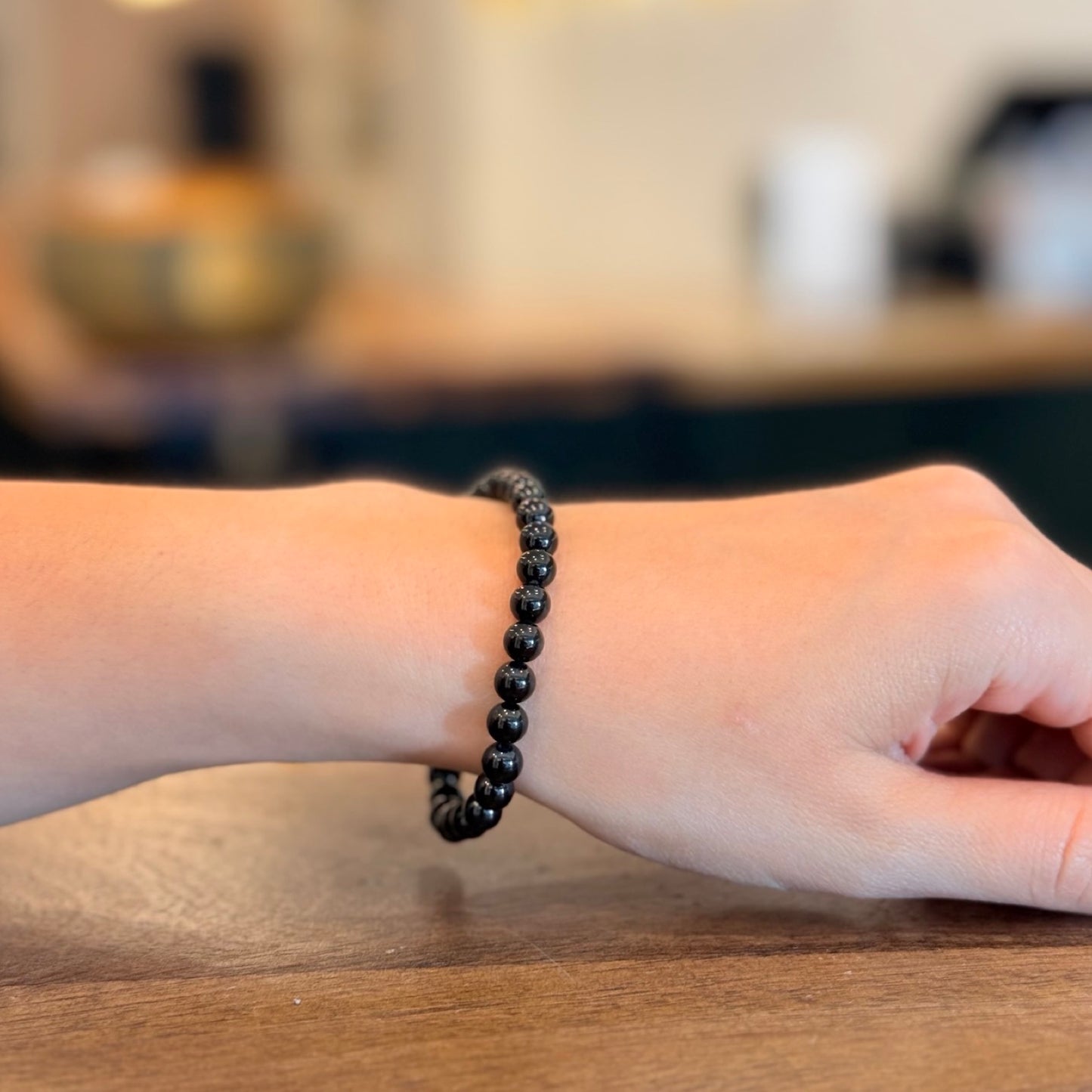 Woman wearing a black tourmaline bracelet on a wooden surface with a blurred background