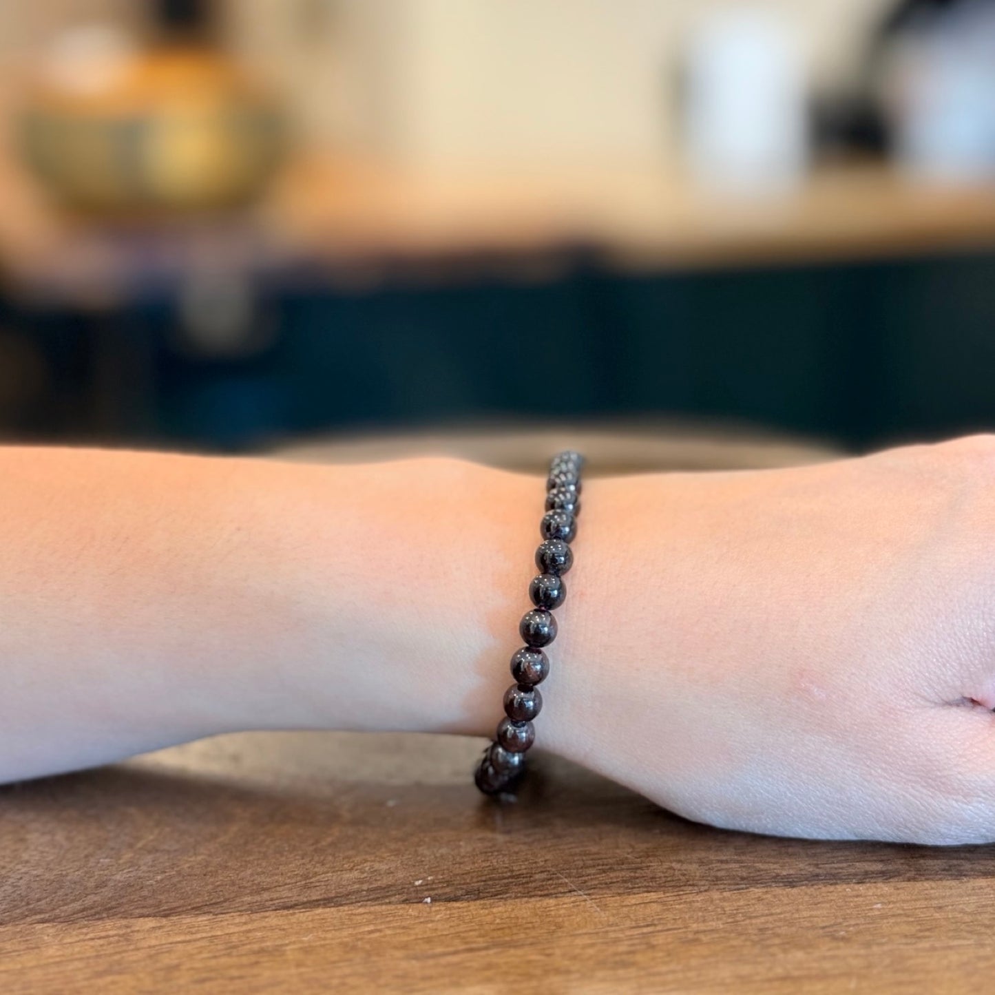 Woman wearing a garnet bracelet on a wooden surface with a blurred background