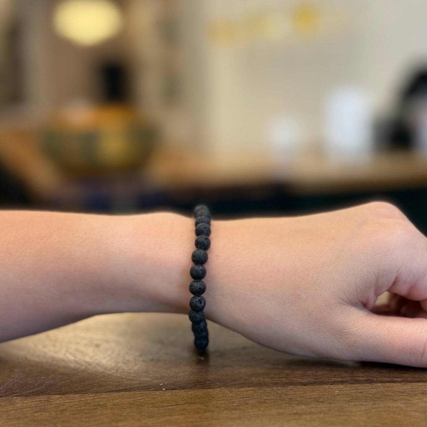 Woman wearing a Lava Stone bracelet on a wooden surface with a blurred background