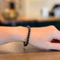 Woman wearing a black tourmaline bracelet on a wooden surface with a blurred background