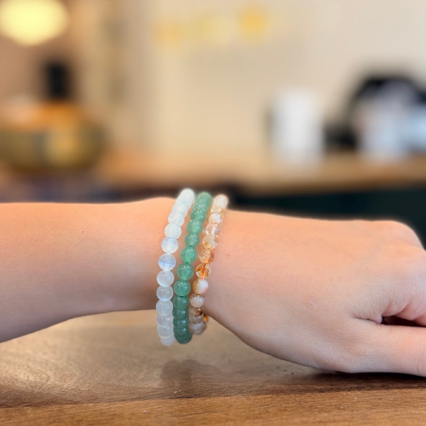 Green Aventurine, Citrine, Selenite bracelets on a wrist with a blurred inside Crystals and Candle store